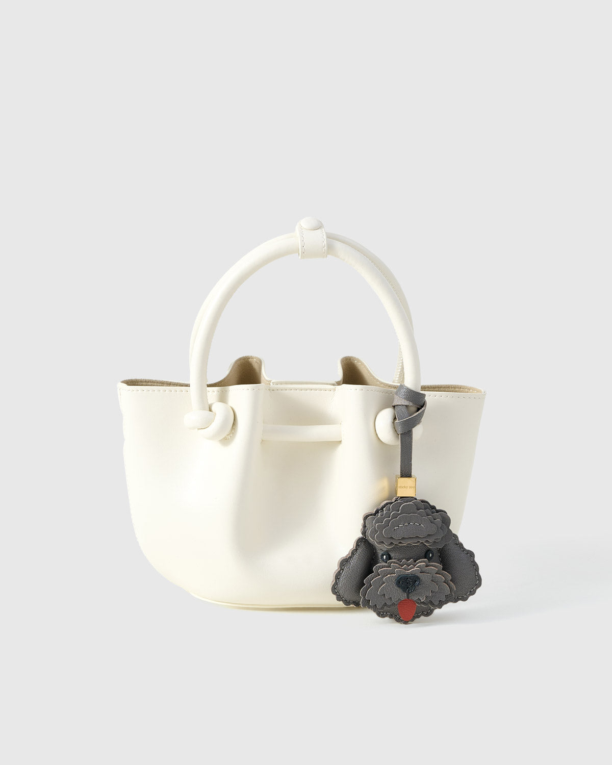 Close-up of handmade Poodle leather bag charm — hand-stitched visible edges on French Alran goatskin, 18K gold-plated cube hardware. STICKYZOO.