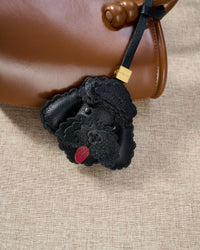 Close-up of handmade Poodle leather bag charm — hand-stitched visible edges on French Alran goatskin, 18K gold-plated cube hardware. STICKYZOO.