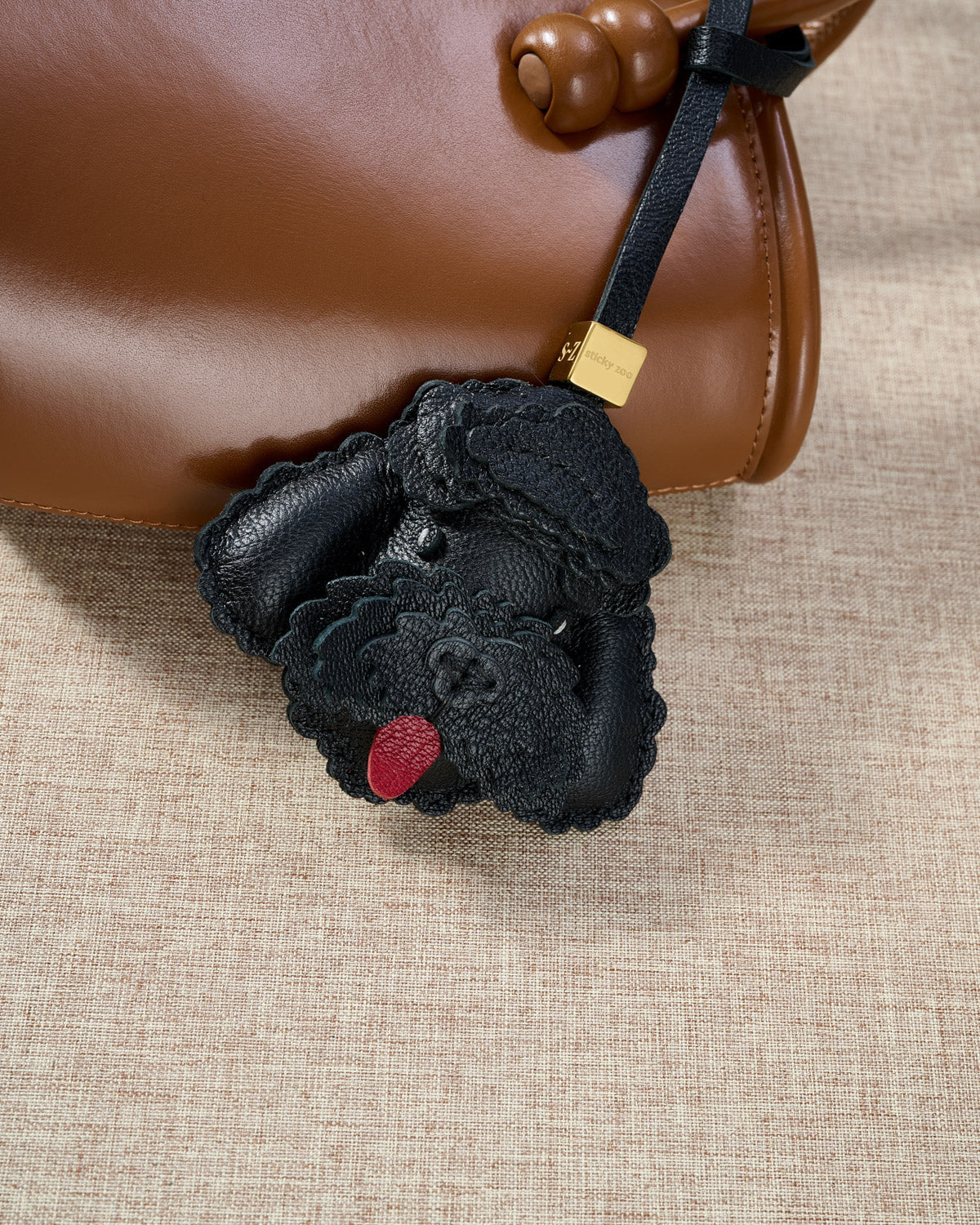 Close-up of handmade Poodle leather bag charm — hand-stitched visible edges on French Alran goatskin, 18K gold-plated cube hardware. STICKYZOO.