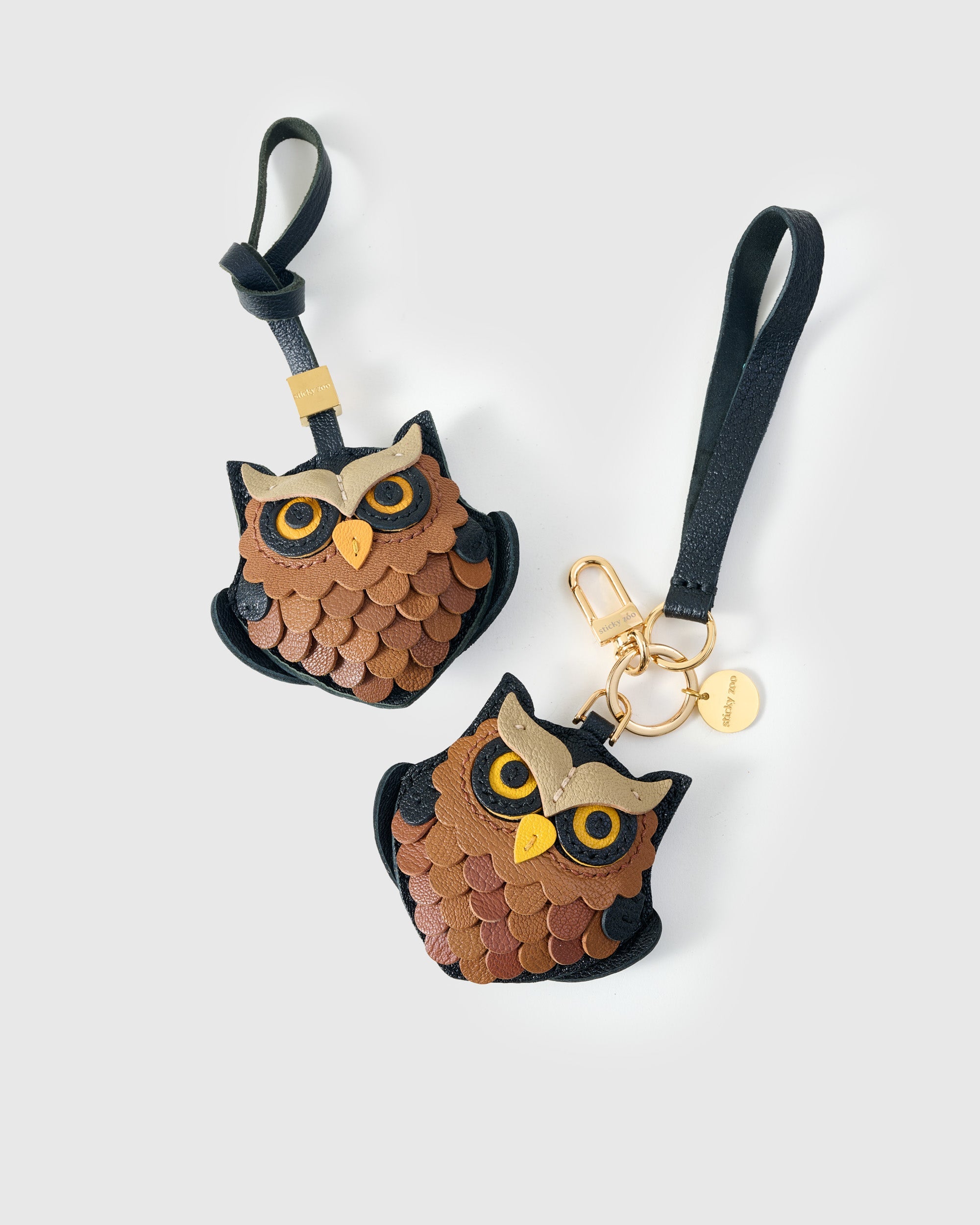 Both editions of the owl charm side by side — leather strap loop for bags, or 18K gold-plated keychain clip.