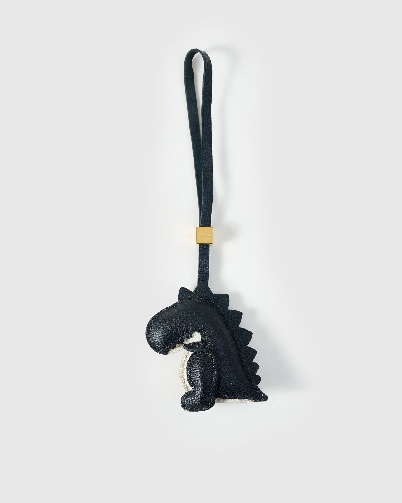 Black dinosaur charm handmade from French Alran genuine goatskin — deep black body, cream belly, hand-cut spine ridges along the back, black leather strap. Three days by hand. Designed in Amsterdam.