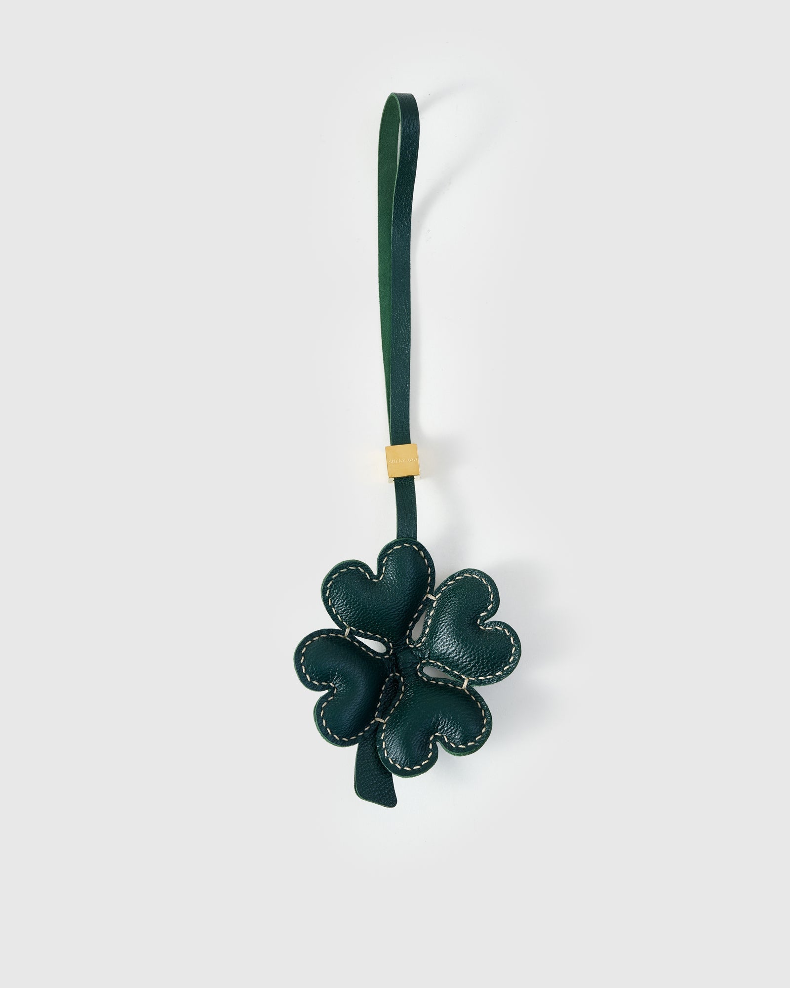 STICKYZOO Lucky Clover Charm in forest-green French Alran goatskin — four padded heart-shaped petals with contrast cream stitching, gold-plated hardware. 3-day handmade piece.