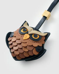 Tight close-up of the owl face — hand-cut scalloped feathers in copper and tan, cream eyebrow, yellow eyes with dark pupils. Every panel by hand.