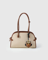 Owl charm styled on a cream canvas-and-tan top-handle bag, front — a small, specific piece that turns a simple bag into a personal one.