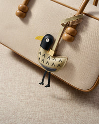 Gull charm styled on a bag, front — a small, specific piece that turns a simple bag into a personal one.