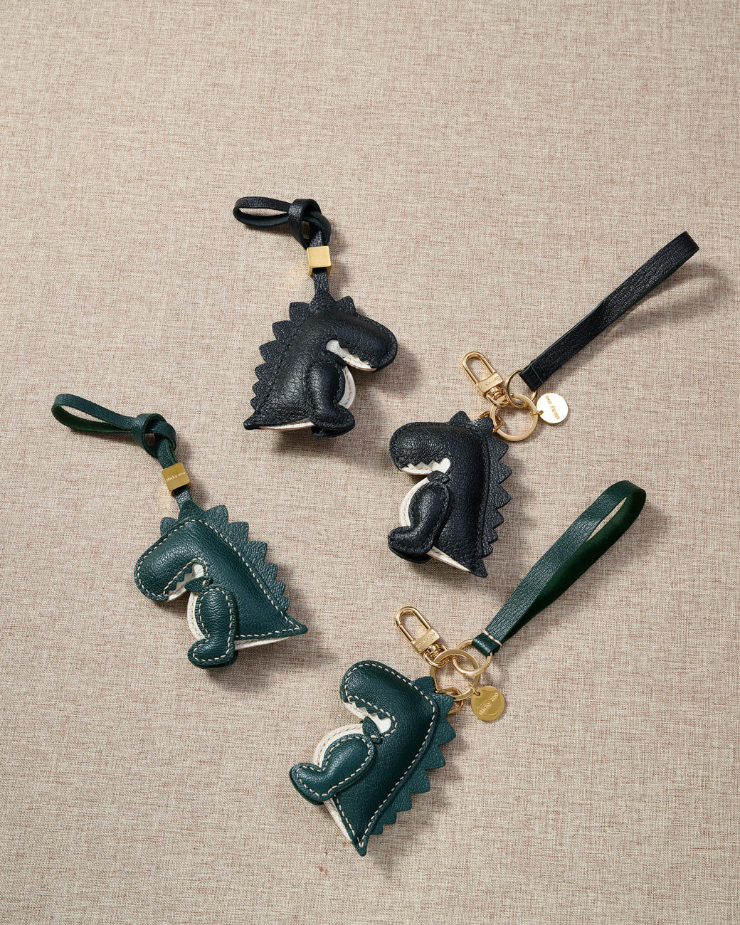 Close-up of the green dinosaur — hand-cut spine ridges along the back, cream belly, cream stitching. Every panel by hand.