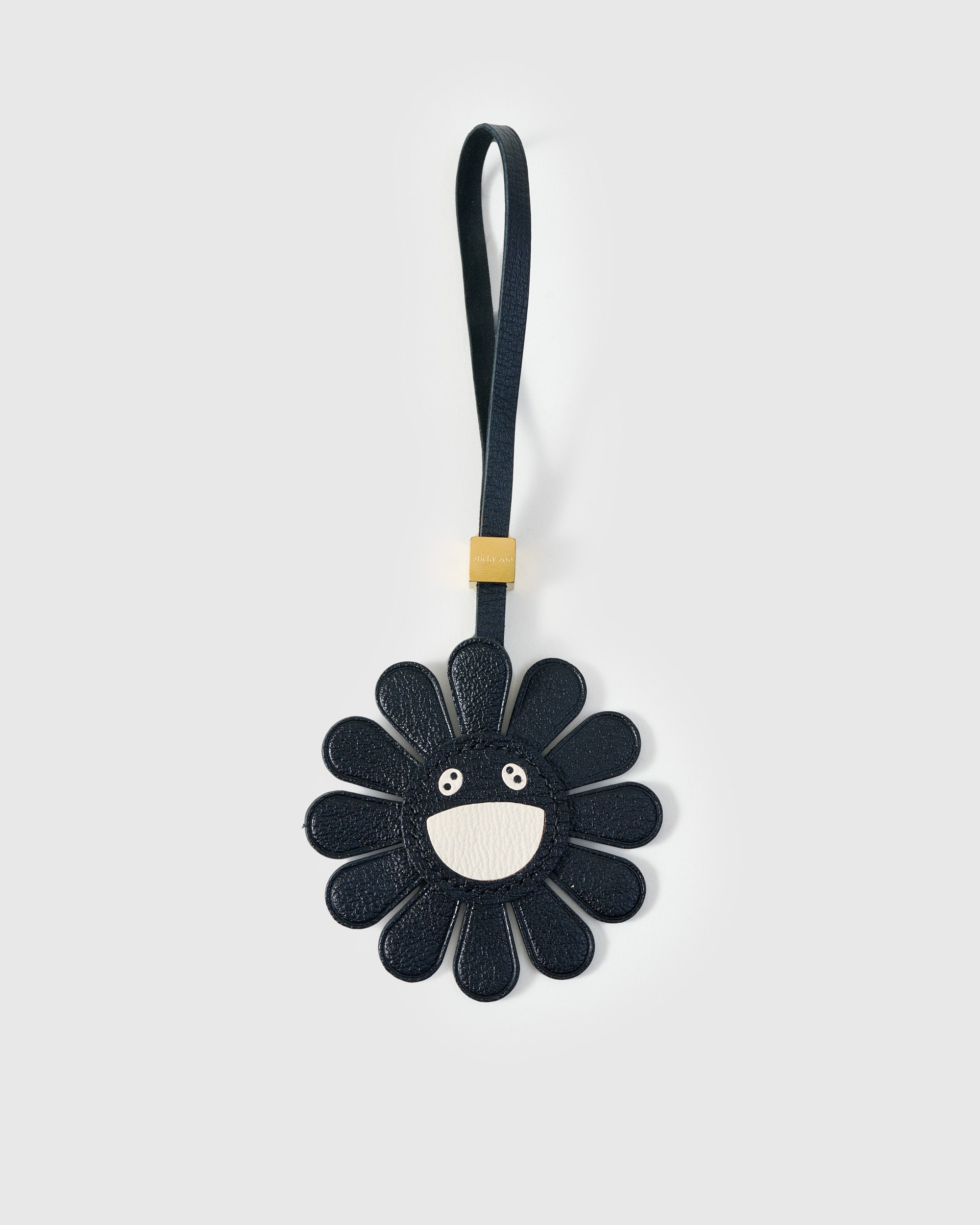STICKYZOO Night Flower Charm — black French Alran goatskin petals with cream smiley face centre, gold-plated hardware. 3-day handmade piece.