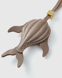 Both editions of the taupe whale — leather strap loop for bags, or 18K gold-plated keychain clip.