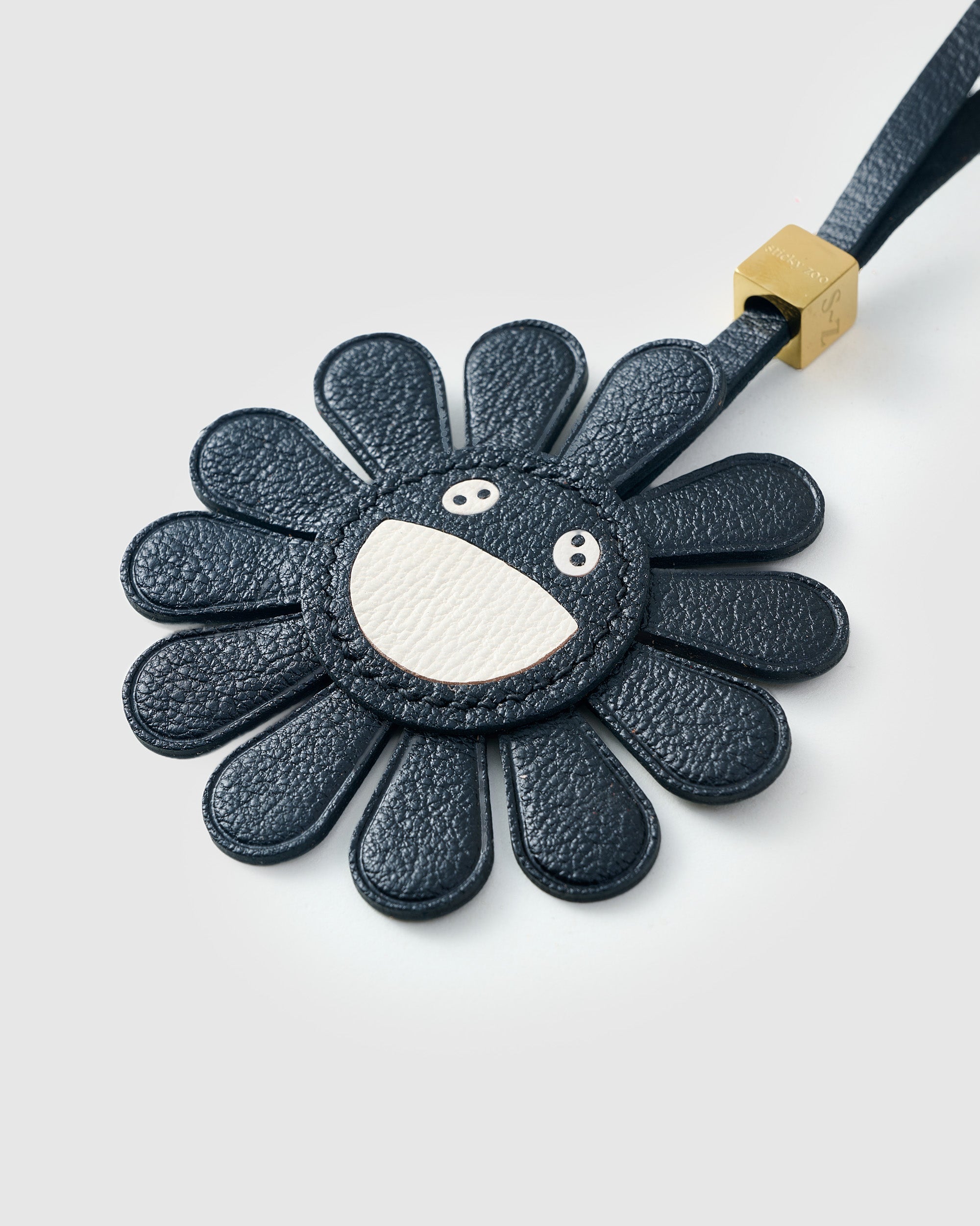 STICKYZOO Night Flower Charm — hand-layered French Alran goatskin, black petals with smiley face centre. Designed in Amsterdam.