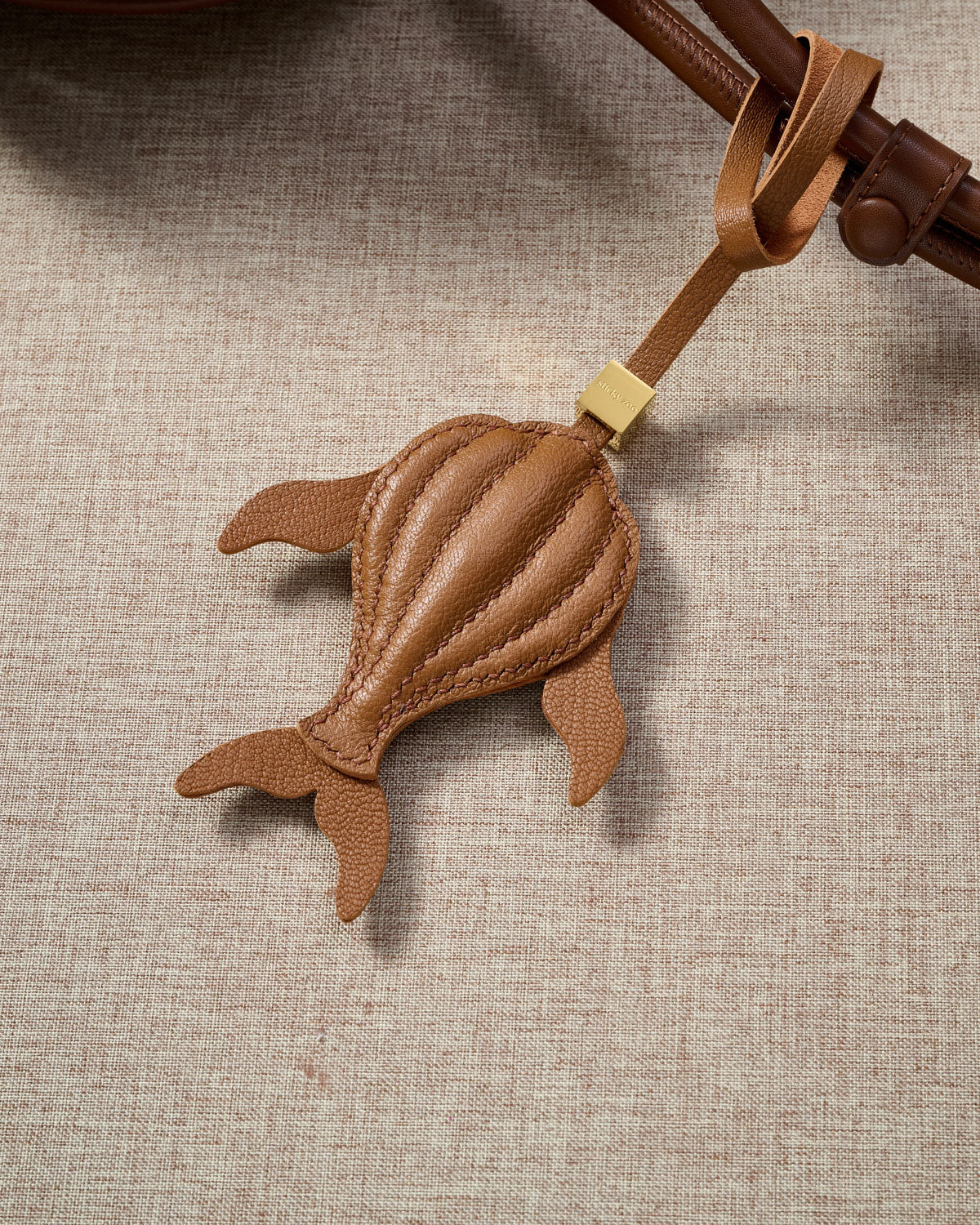 Caramel whale charm styled on a bag, front — a small, specific piece that turns a simple bag into a personal one.