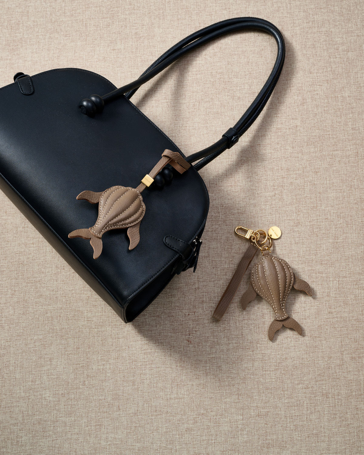 Close-up of the taupe whale — cream hand-stitched seams running along the 3D body, side fins and split tail. Every panel by hand.