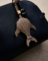 Taupe whale charm styled on a bag, front — a small, specific piece that turns a simple bag into a personal one.