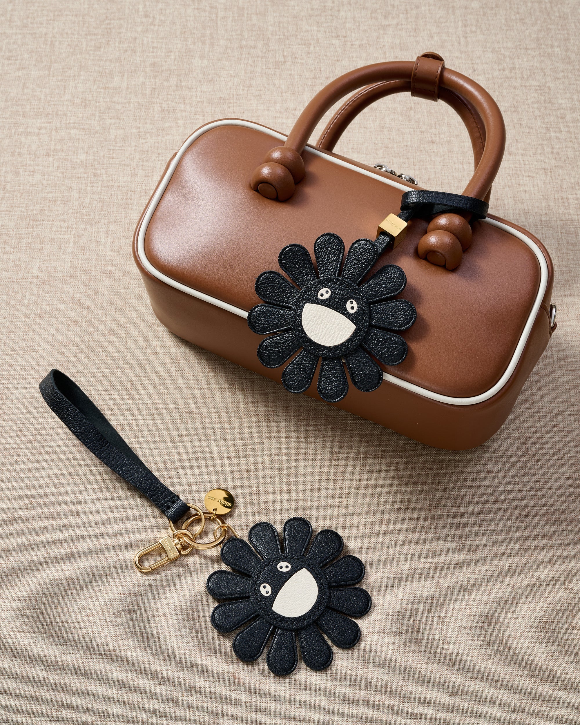 STICKYZOO Night Flower Charm — hand-cut, hand-stitched black petals with smiley face centre in French Alran goatskin. Designed in Amsterdam.