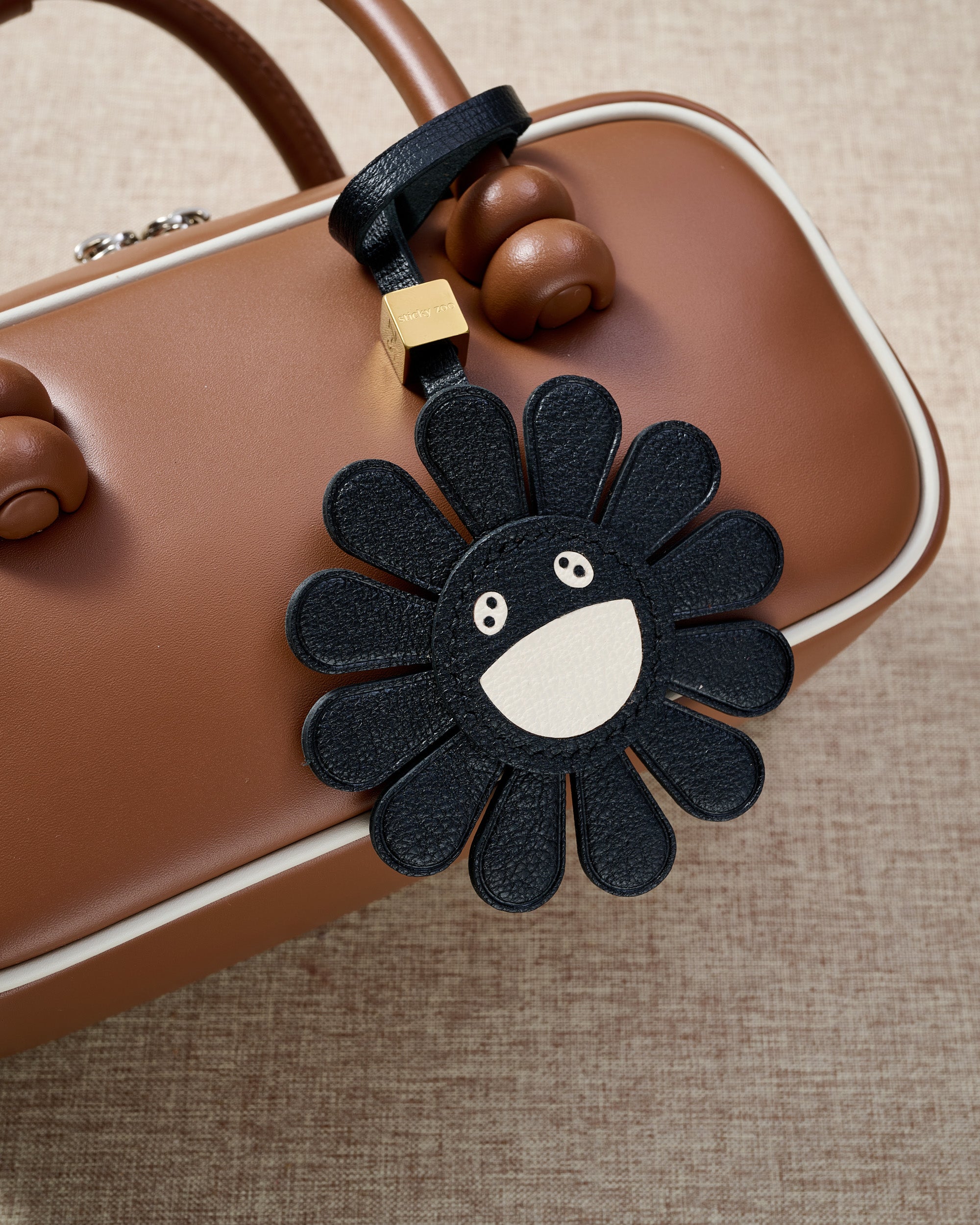 Close-up of STICKYZOO Night Flower Charm — full-grain French Alran goatskin from Tarn, France. Black petals with smiley face centre. 3-day handmade piece.