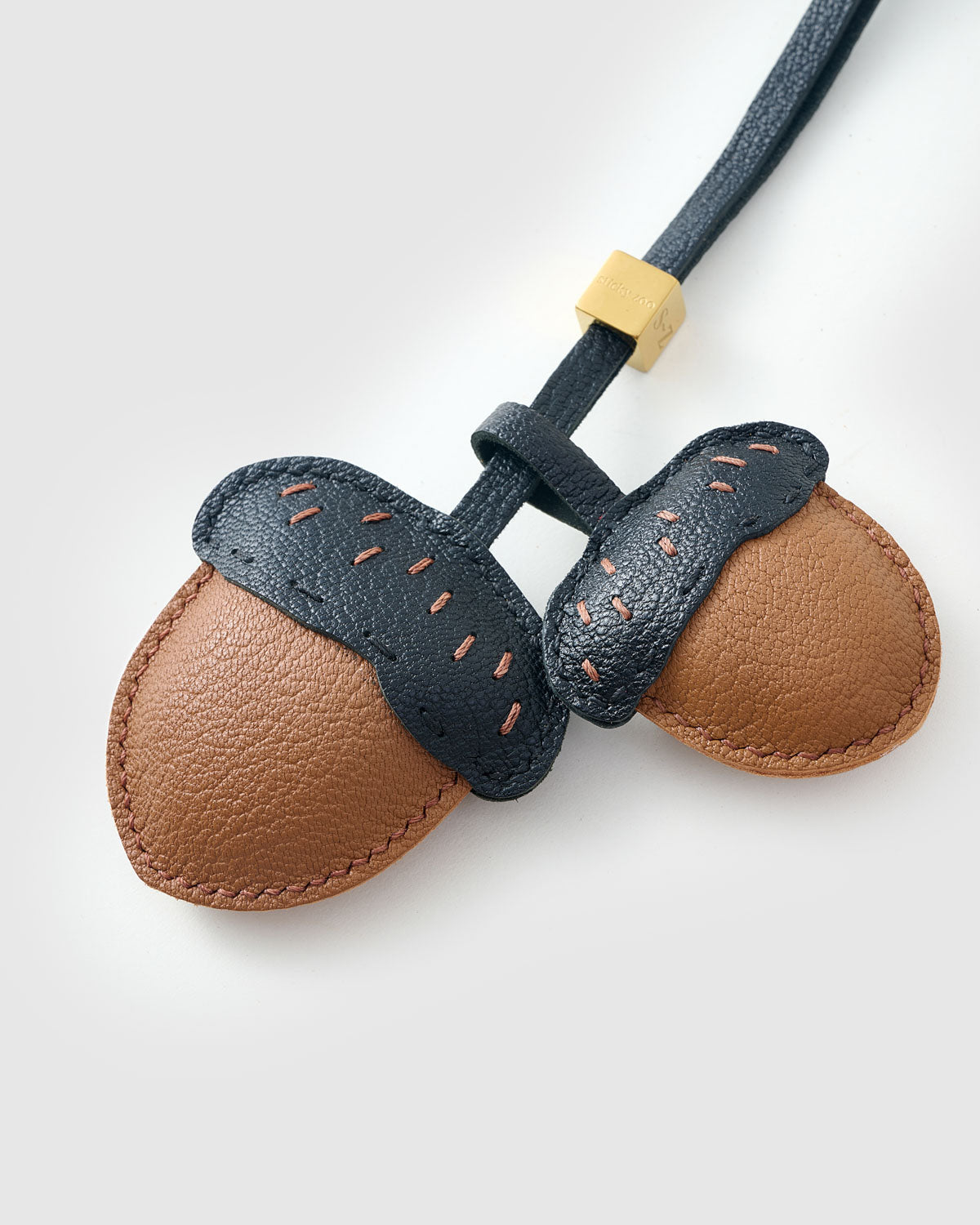 STICKYZOO Acorns Charm clipped to a handbag — handmade French Alran goatskin in warm tan with dark navy caps. 3-day artisan build.