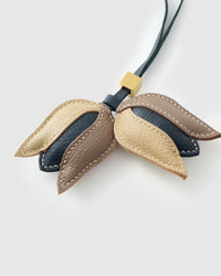 STICKYZOO Tulip Charm clipped to a handbag — handmade French Alran goatskin in gold, taupe, and dark. 3-day artisan build.