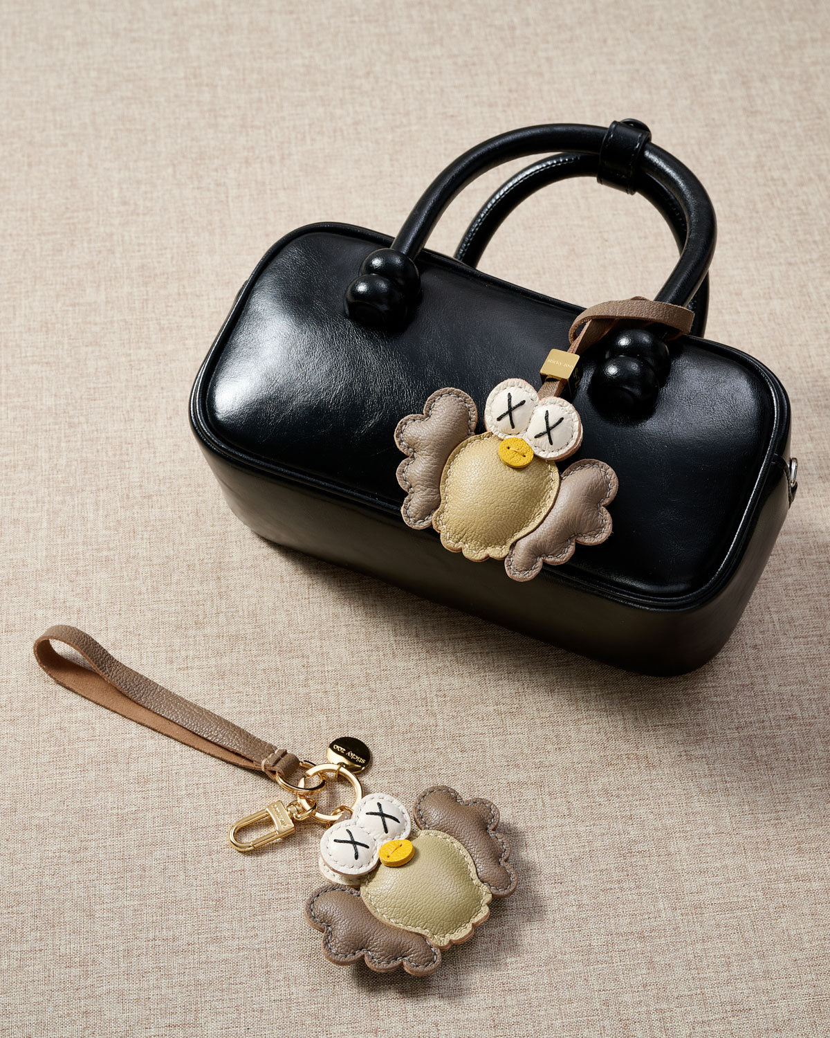 Gold Hootie charm styled on a bag, front — a small, specific piece that turns a simple bag into a personal one.