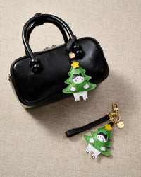 Both editions of the kitten in Christmas tree charm side by side — leather strap loop for bags, or 18K gold-plated keychain clip with engraved STICKYZOO disc.