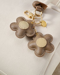 STICKYZOO Twin Flowers Charm — hand-cut, hand-stitched twin five-petal blooms on gold keychain in French Alran goatskin. Designed in Amsterdam.