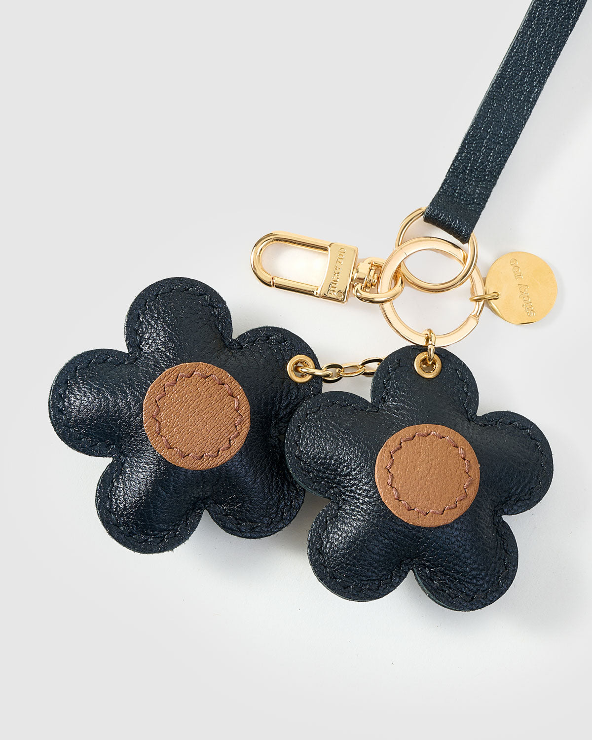 Close-up of STICKYZOO Twin Flowers Charm — full-grain French Alran goatskin from Tarn, France. Twin five-petal blooms on gold keychain. 3-day handmade piece.