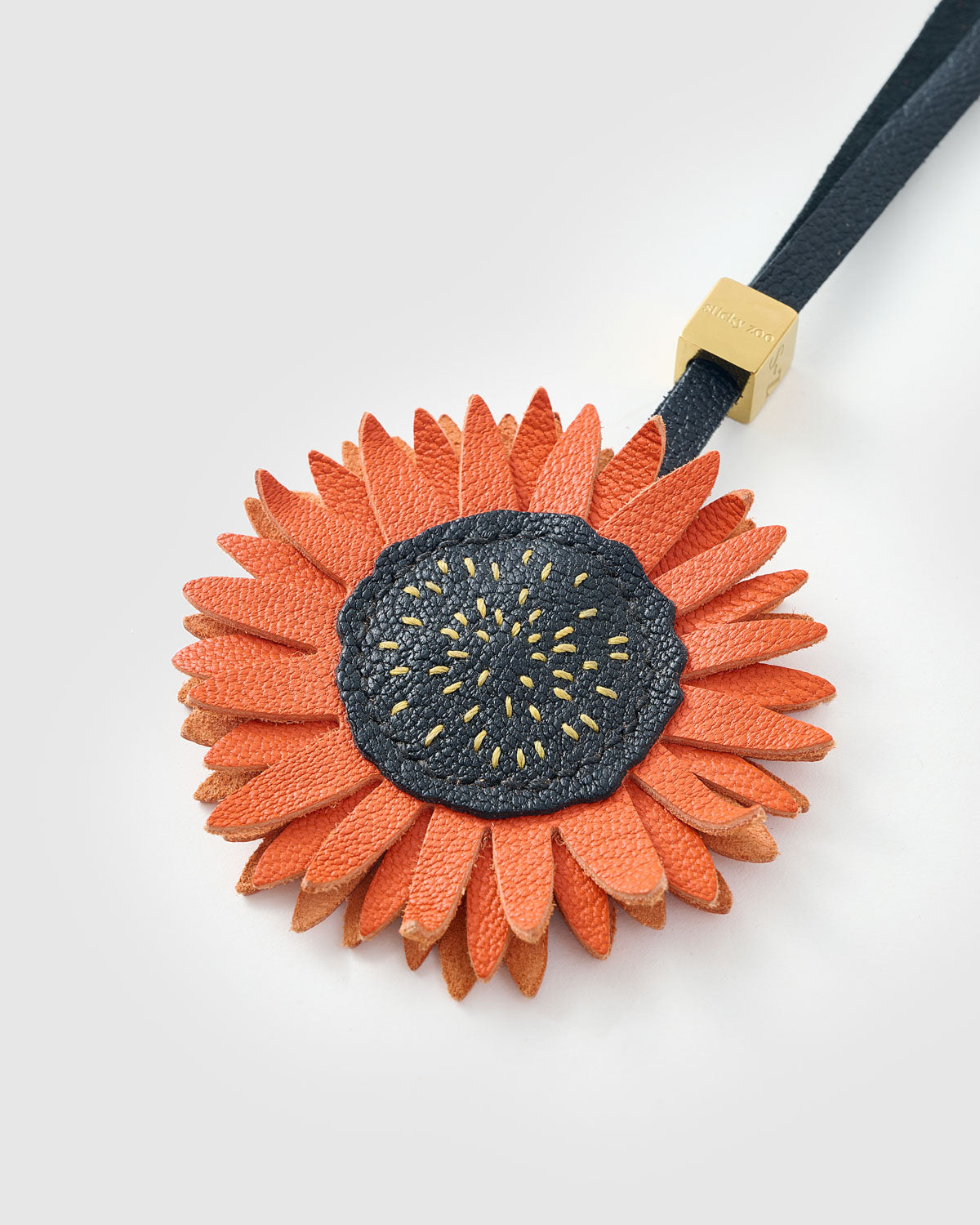 STICKYZOO Sunflower Charm clipped to a handbag — handmade French Alran goatskin in rust orange over dark navy. 3-day artisan build.