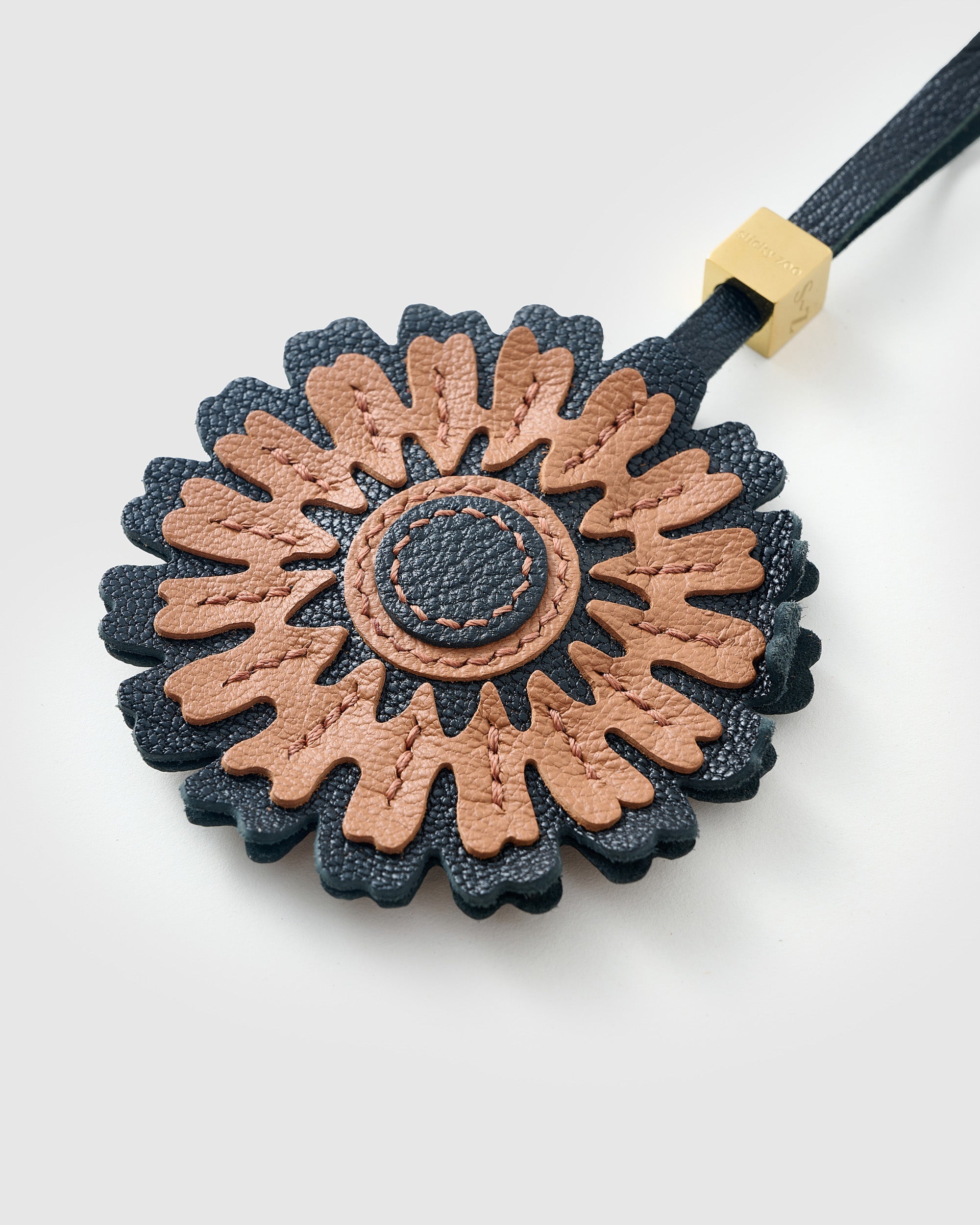 STICKYZOO Sunflower Charm clipped to a handbag — handmade French Alran goatskin in caramel over dark navy. 3-day artisan build.
