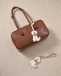 Close-up of handmade Golden Retriever leather bag charm — hand-stitched visible edges on French Alran goatskin, 18K gold-plated cube hardware. STICKYZOO.