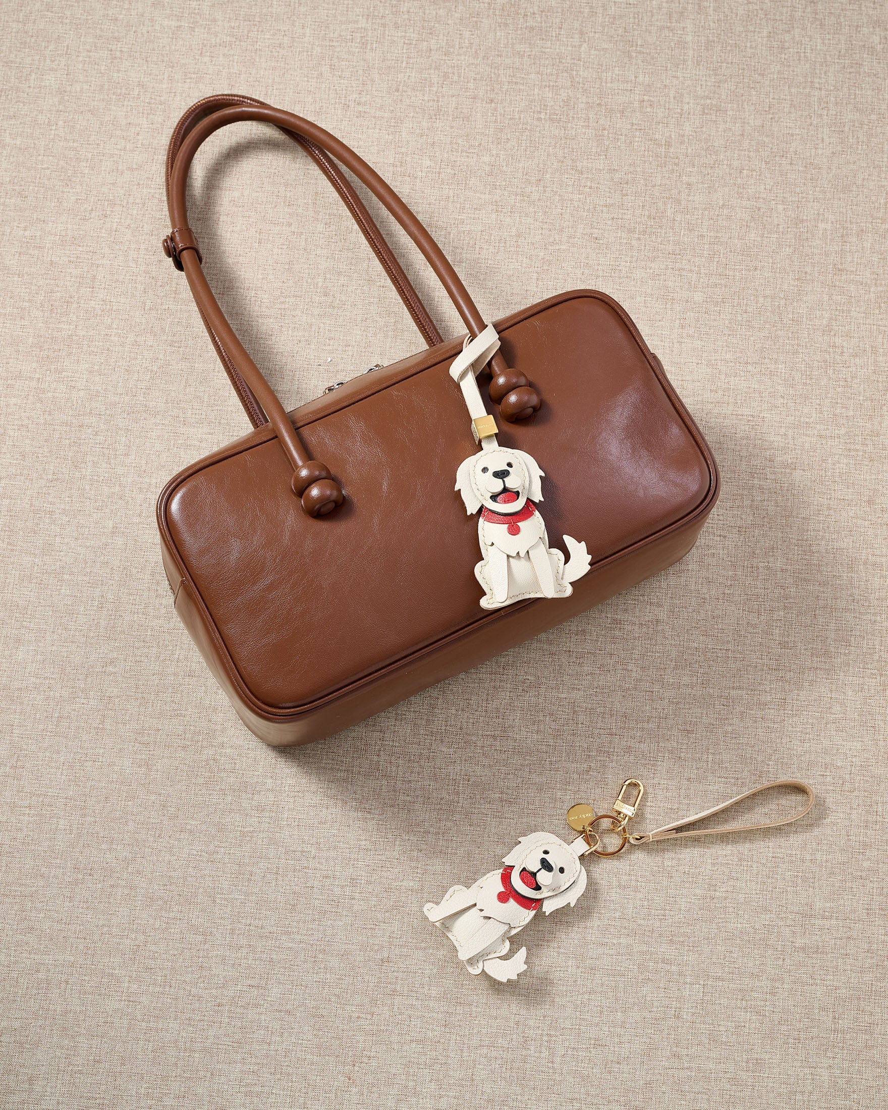 Close-up of handmade Golden Retriever leather bag charm — hand-stitched visible edges on French Alran goatskin, 18K gold-plated cube hardware. STICKYZOO.