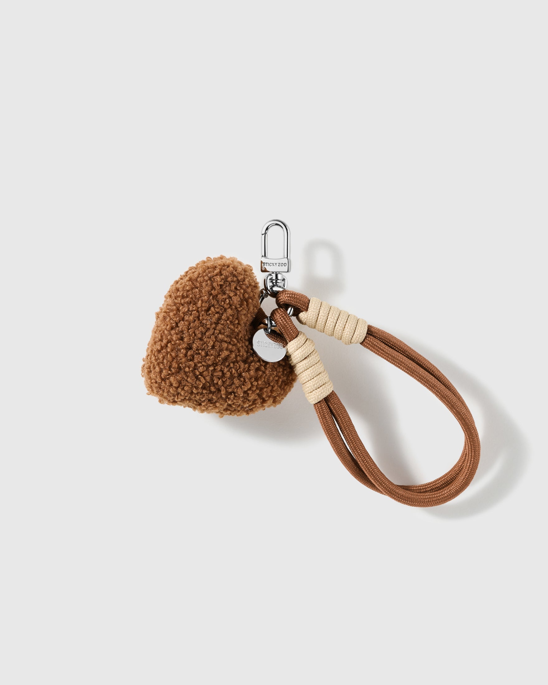 Cocoa Pom-Pom Wristlet Charm with a plush brown pom-pom sits beside a loop made from coordinated brown and cream cords on a light background