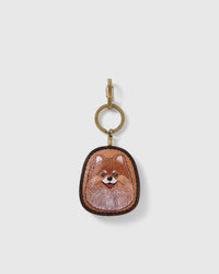 STICKYZOO Posie Pomeranian portrait charm with a smiling warm tan and cream face, dark stitched border, and gold-tone ring-and-clip hardware on a pale background