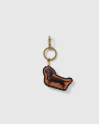 STICKYZOO Penny Dachshund portrait charm with a long espresso-brown dog profile on a warm tan panel, visible dark edge stitching, and gold-tone ring-and-clip hardware on a pale background