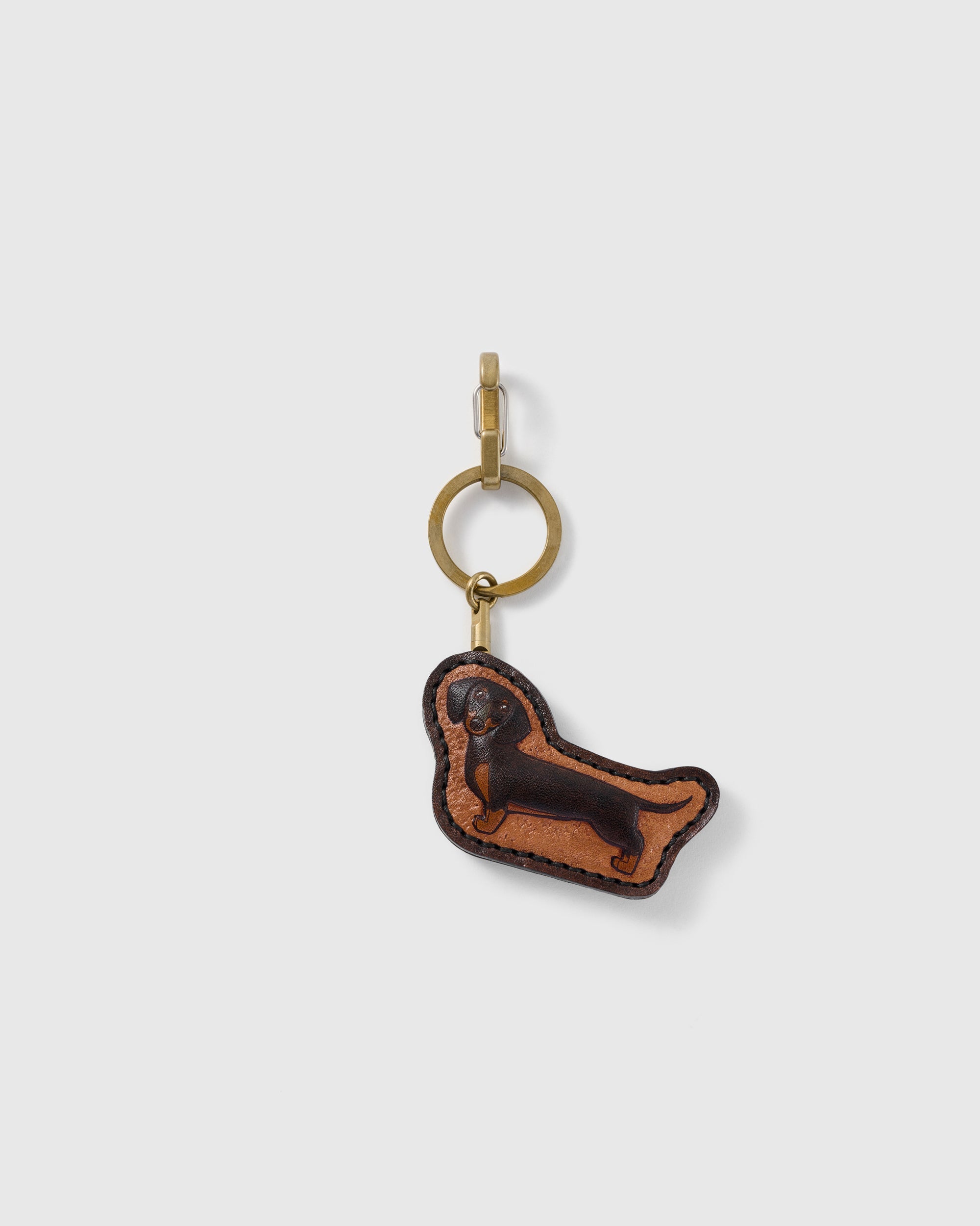 STICKYZOO Penny Dachshund portrait charm with a long espresso-brown dog profile on a warm tan panel, visible dark edge stitching, and gold-tone ring-and-clip hardware on a pale background