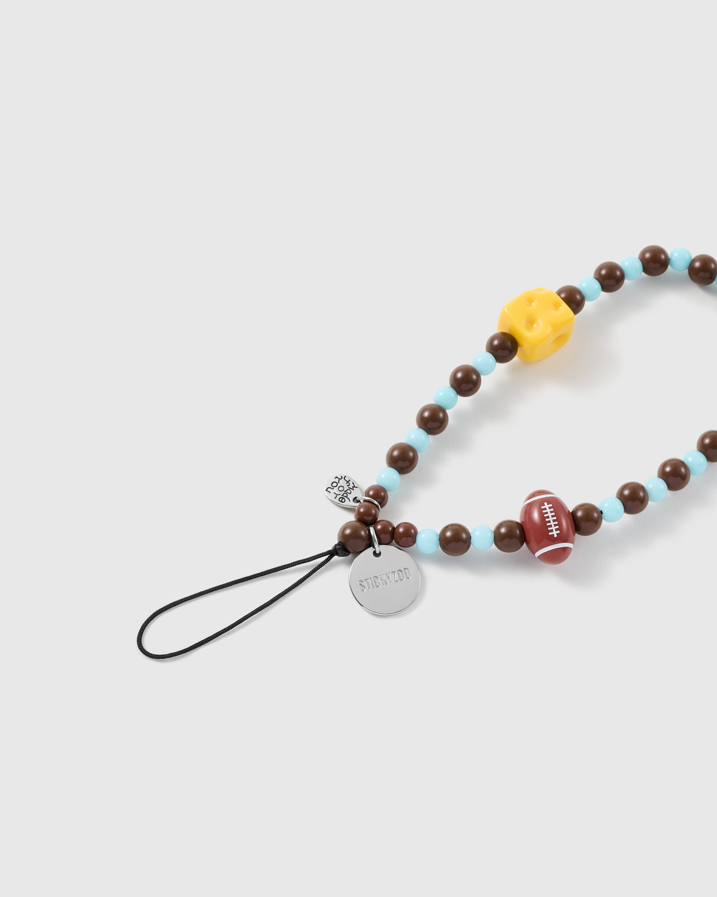 Close view of the football and cheese beads, silver-tone STICKYZOO disc, small heart charm and black attachment loop.