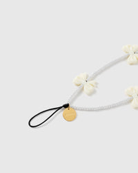 Close view of the ivory bow beads, white faux-pearl strand, engraved gold-tone STICKYZOO disc and attachment loop.