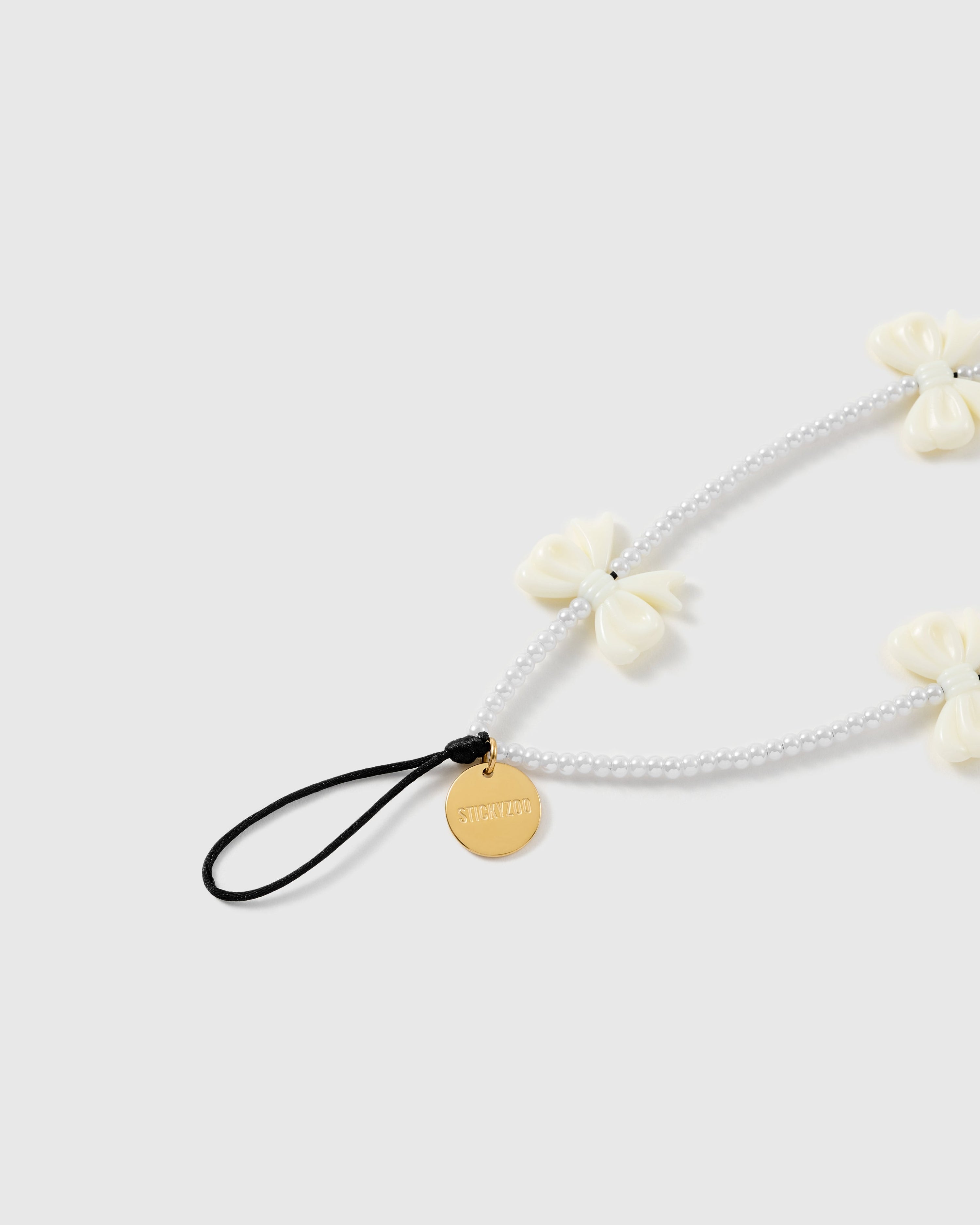 Close view of the ivory bow beads, white faux-pearl strand, engraved gold-tone STICKYZOO disc and attachment loop.