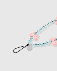 Close-up of the STICKYZOO strap's black stretch-cord loop and engraved silver-tone disc beside glossy pink bows and faceted ice-blue beads