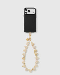 Black triple-camera phone case with the ivory heart bead wrist strap hanging in a loop from a gold hook and engraved gold disc.