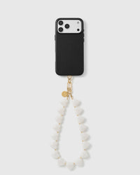 Black phone with the milky white heart bead wrist strap hanging in a soft loop, gold hook and disc at the top.
