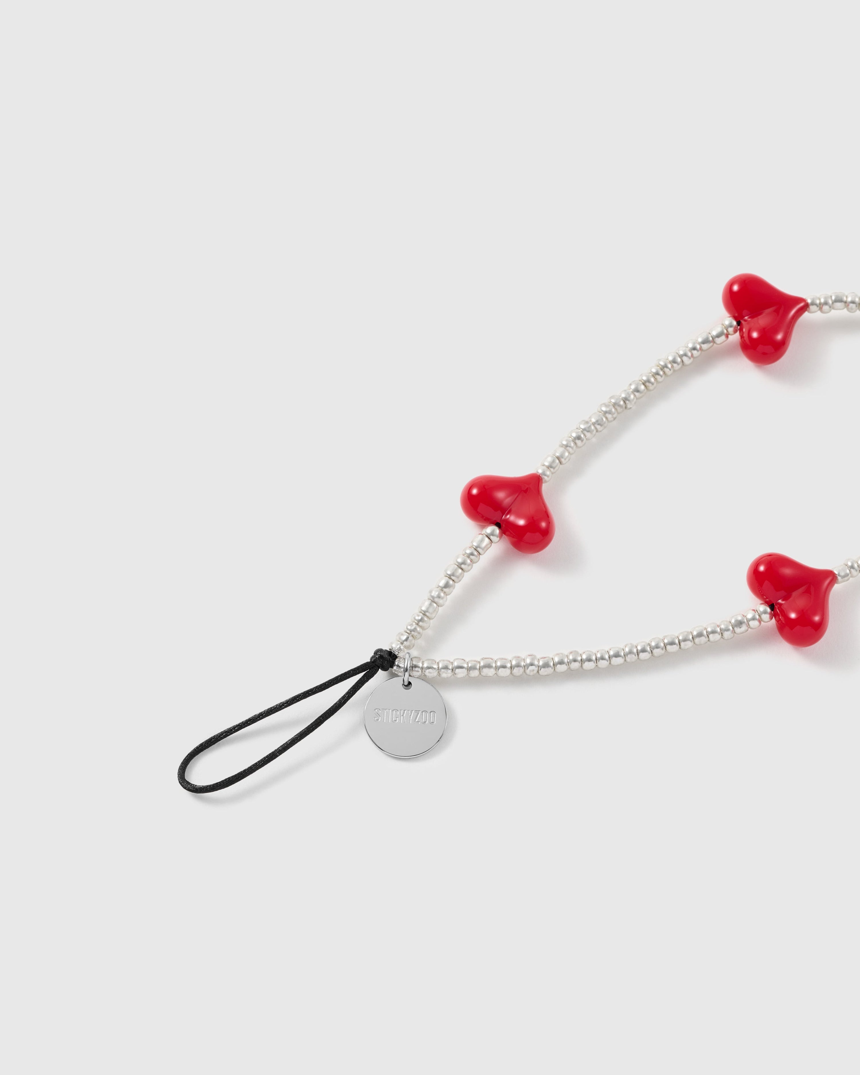 Close view of the red heart beads, silver-tone seed-bead strand, engraved STICKYZOO disc and black attachment loop.