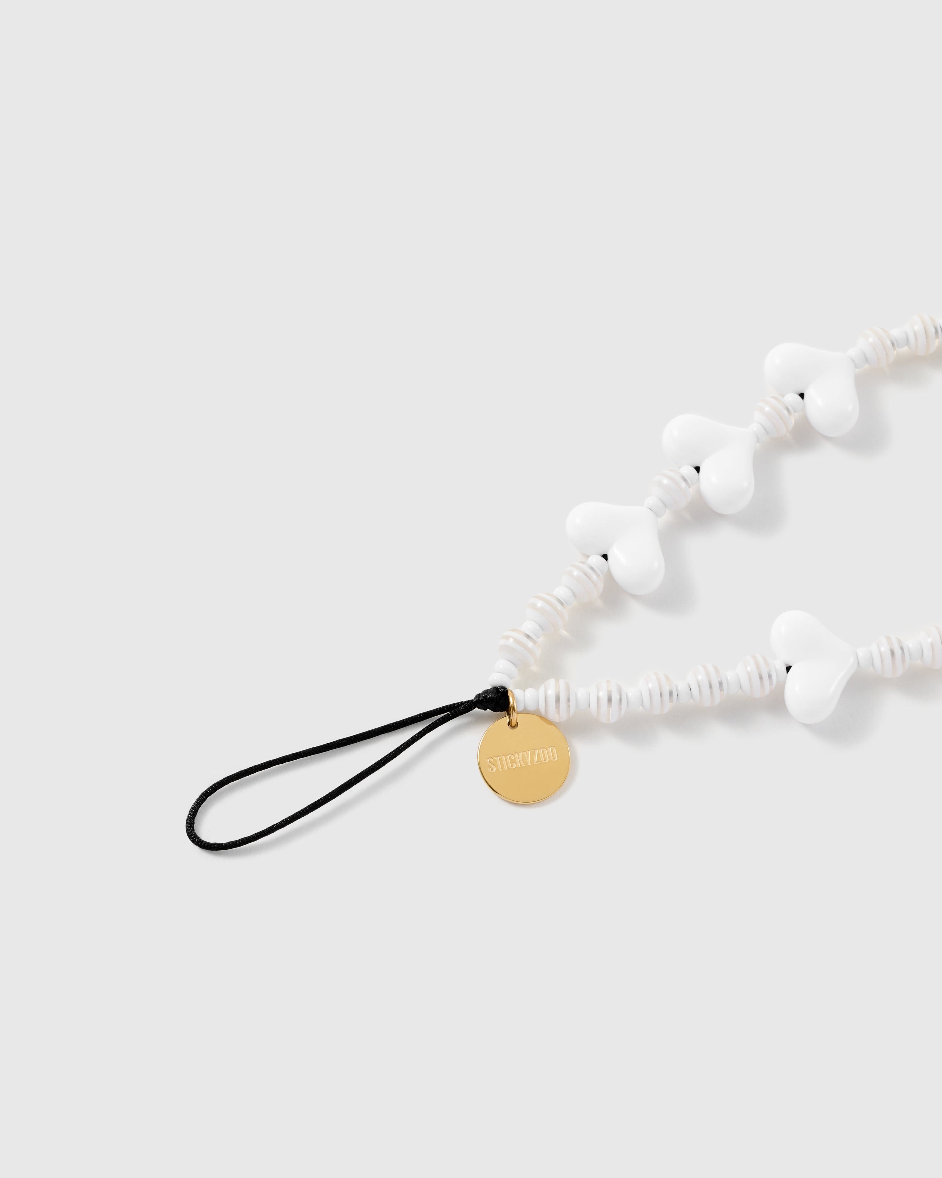 Close view of the glossy white hearts, ribbed disc beads, engraved gold-tone STICKYZOO disc and attachment loop.