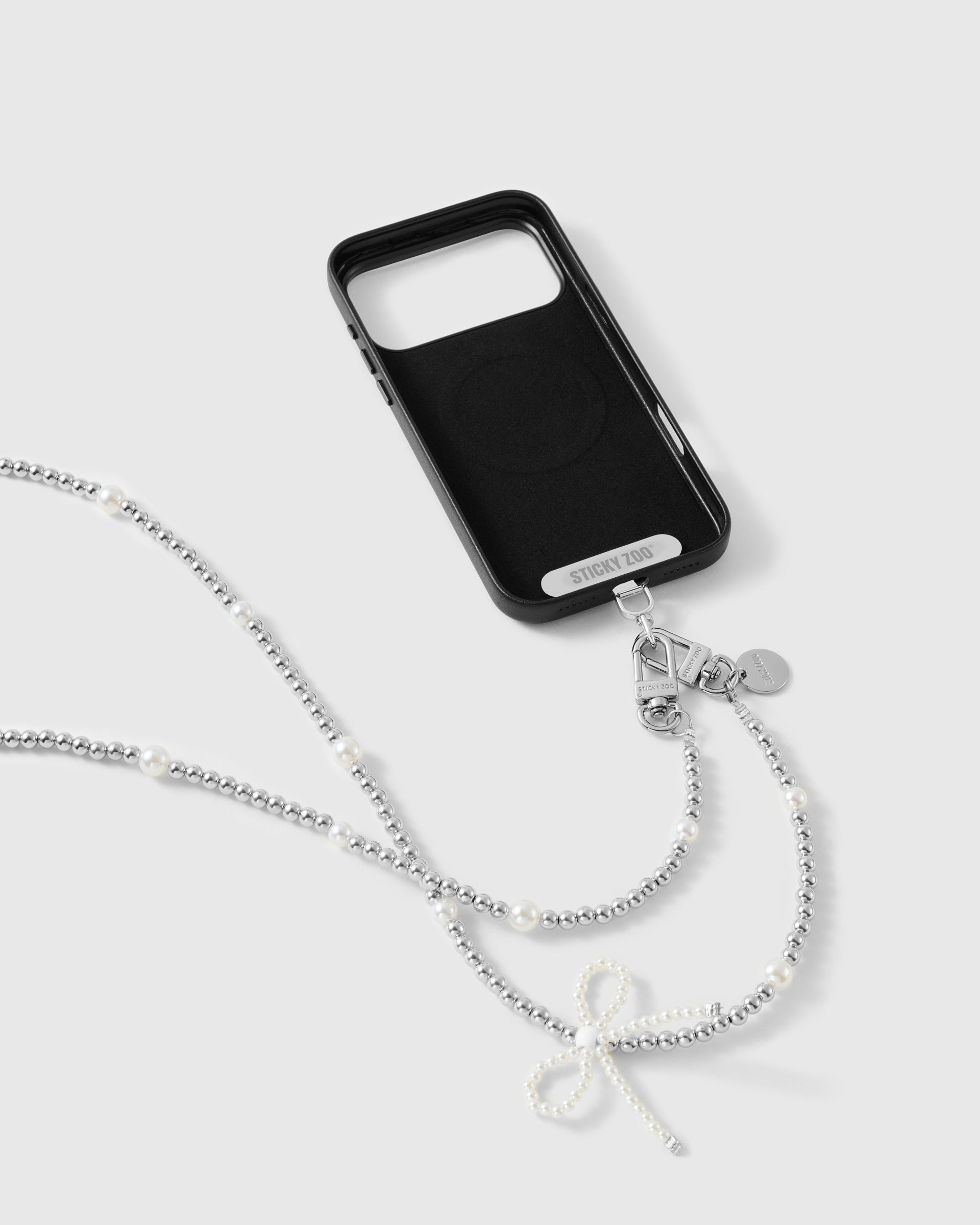 Pearl Bow cross-body phone strap attached to a black case with dual clasps and the included Phone Strap Card.