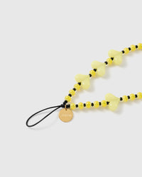 Close-up of the gold-tone STICKYZOO disc on the black stretch-cord loop, beside striped yellow beads and a pale lemon heart bead