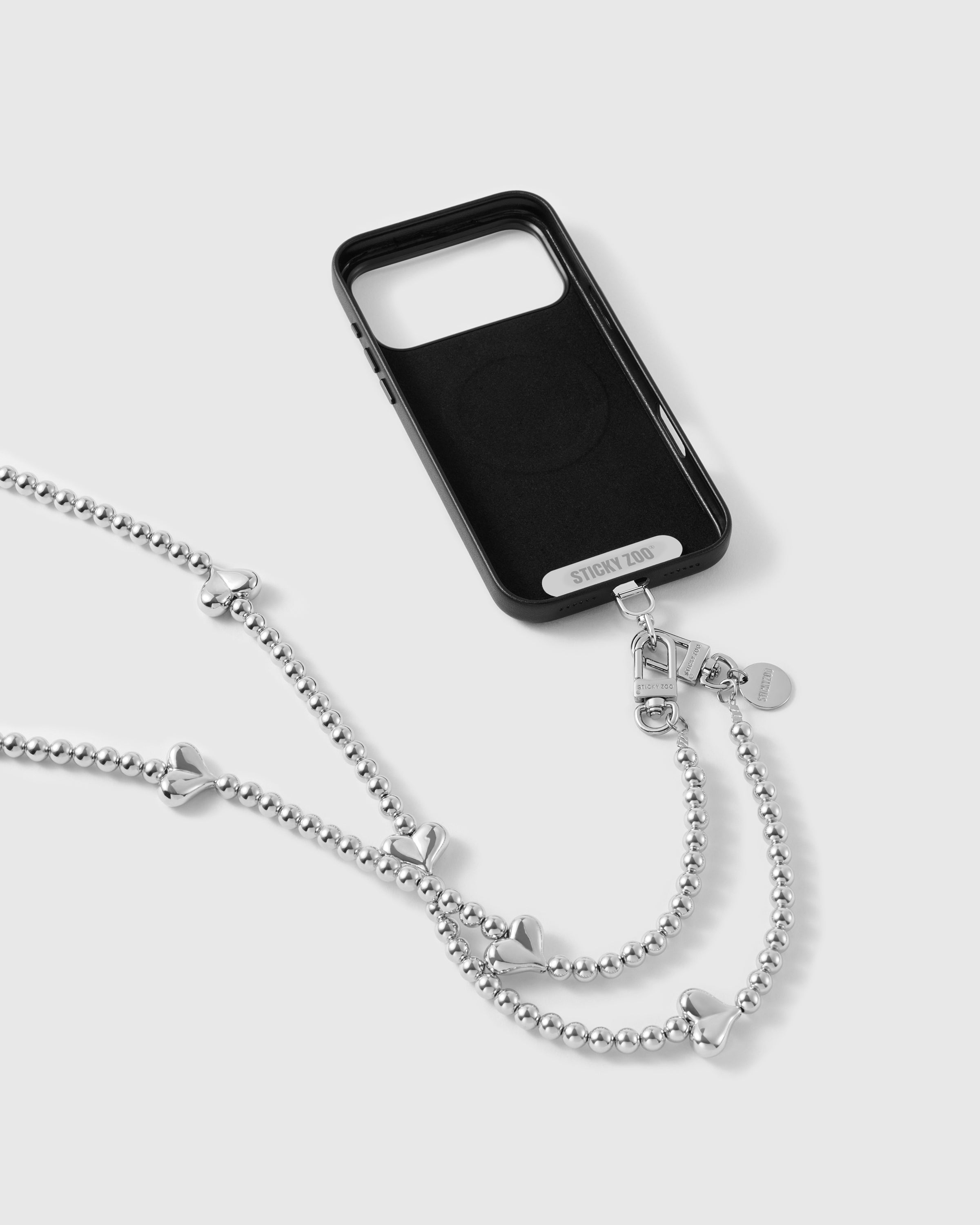 Silver heart cross-body phone strap attached to a black phone case with dual clasps and the included Phone Strap Card.