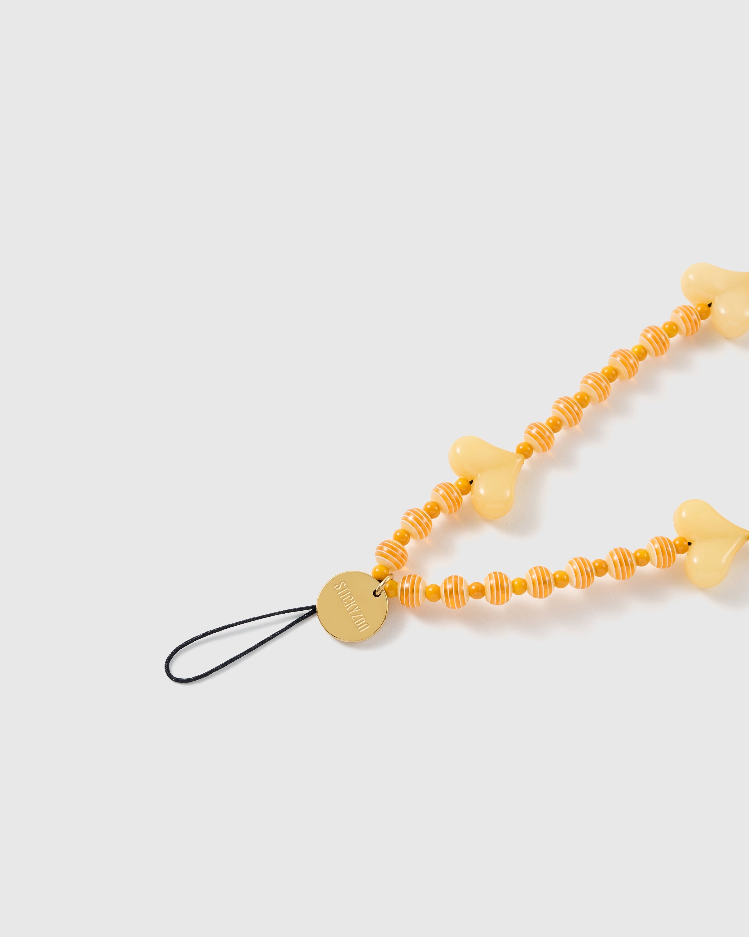 Close view of the yellow heart beads, striped orange-and-cream rounds, gold-tone STICKYZOO disc and black loop.
