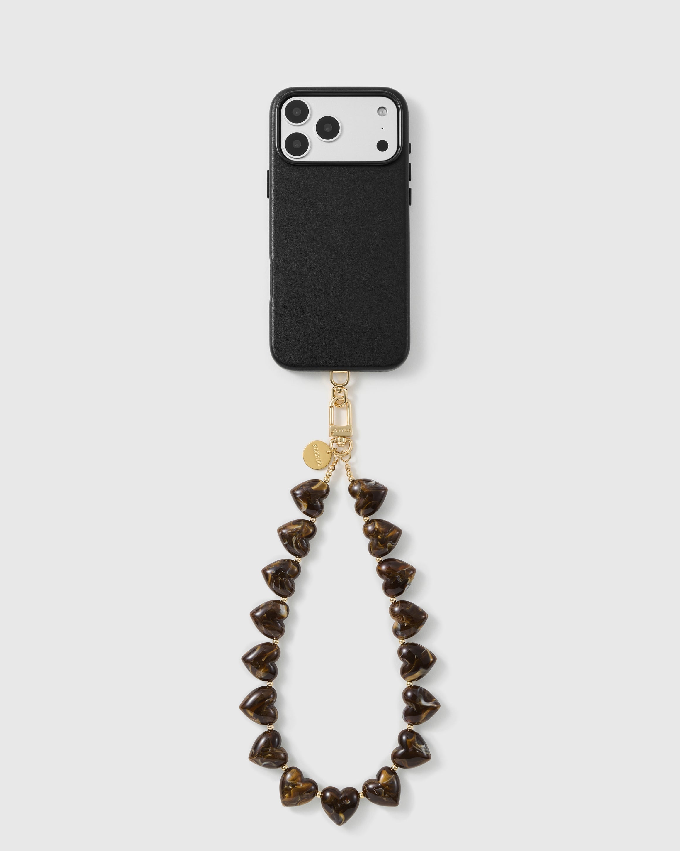Tortoiseshell Heart wrist strap looped below a black phone case, with marbled amber heart beads, a gold-tone hook and engraved disc.