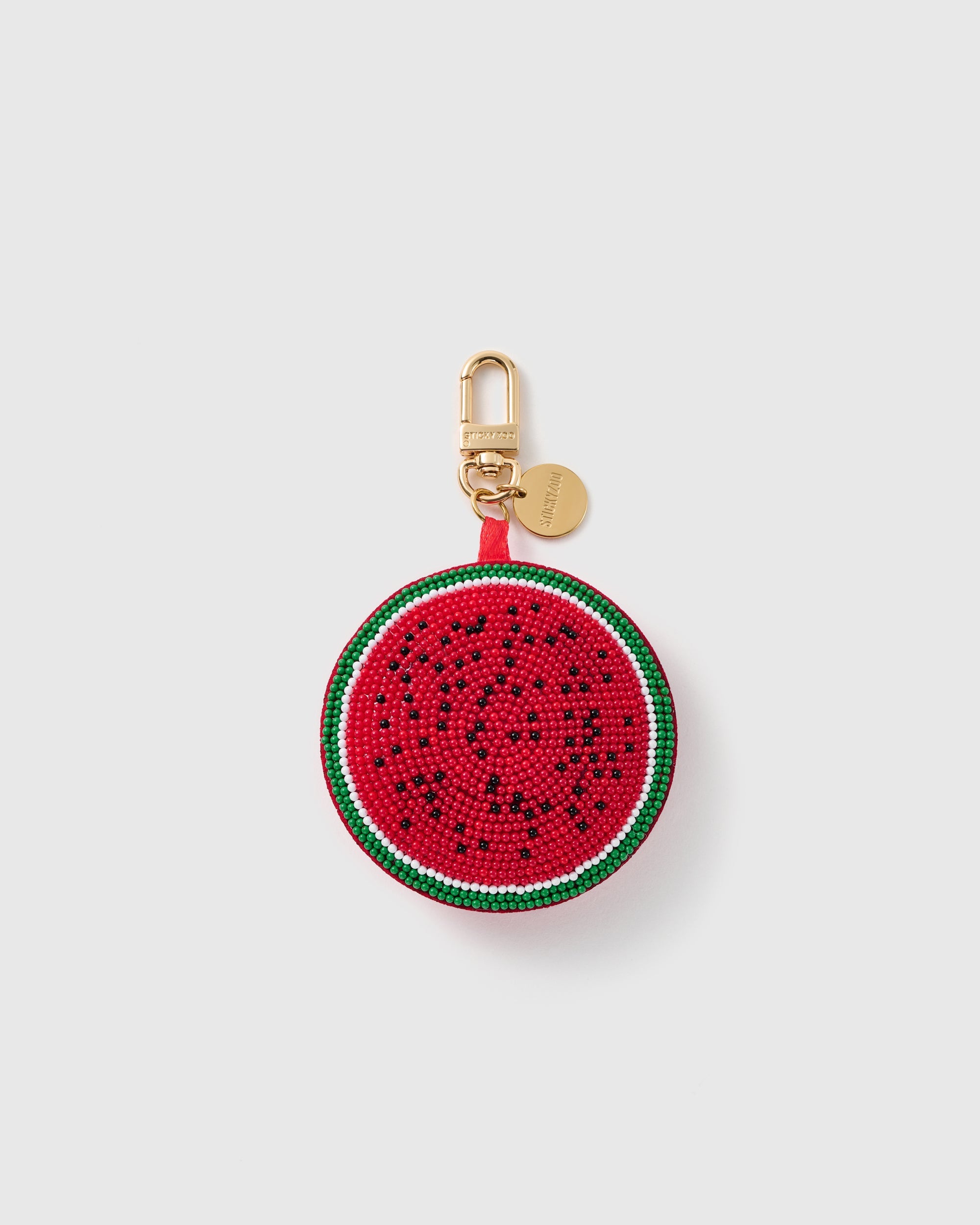 STICKYZOO Luna Watermelon Dot charm with a round red bead-covered center, black seed dots, white rind line, green edge, gold-tone swivel clasp, and engraved tag on a pale background
