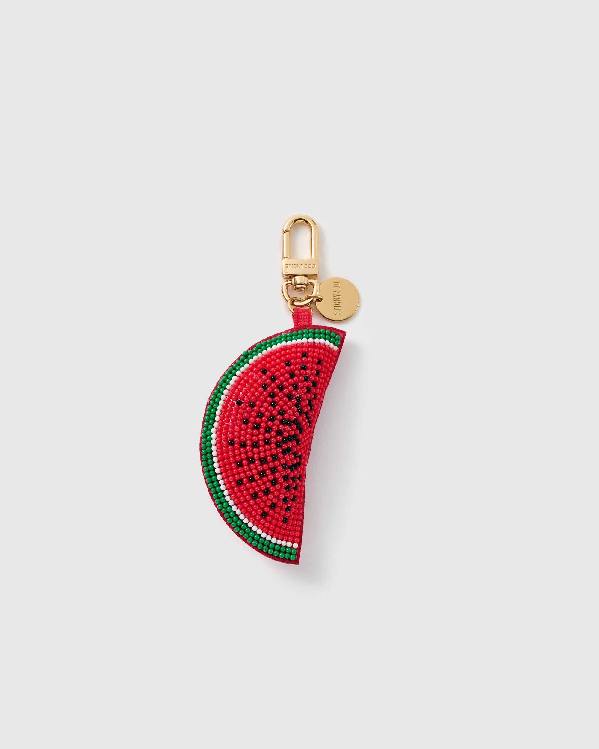 STICKYZOO Lola Watermelon Pop charm with a curved red bead-covered slice, black seed pattern, white rind line, green edge, gold-tone swivel clasp, and engraved tag on a pale background