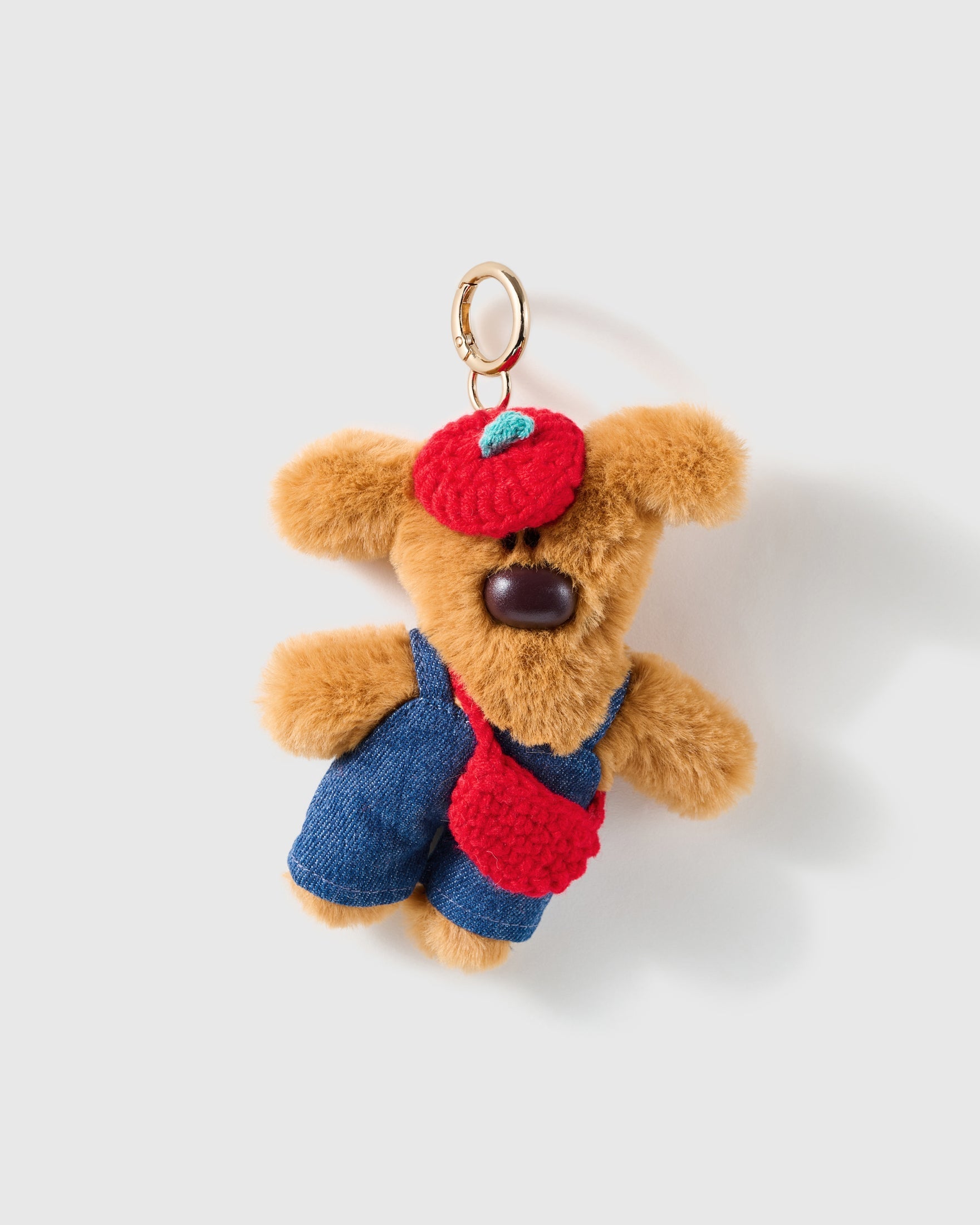 Apple Beret Teddy Charm, tan plush teddy with red apple beret, red pouch and blue overalls, on a light background