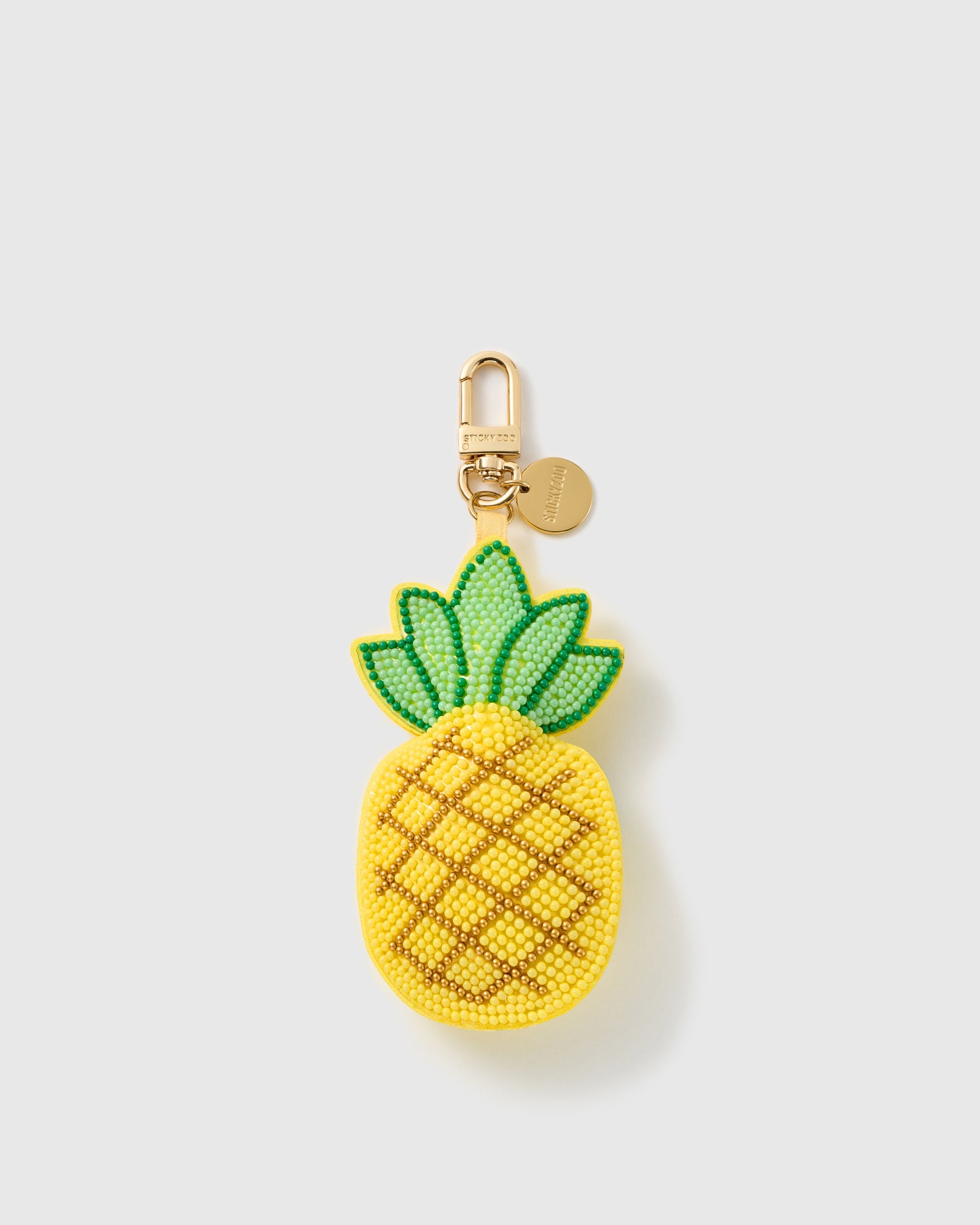 STICKYZOO Penelope Pineapple Fizz charm with yellow bead-covered fruit, gold-tone diamond crosshatch, mint-green crown, gold-tone swivel clasp, and engraved round tag on a pale background