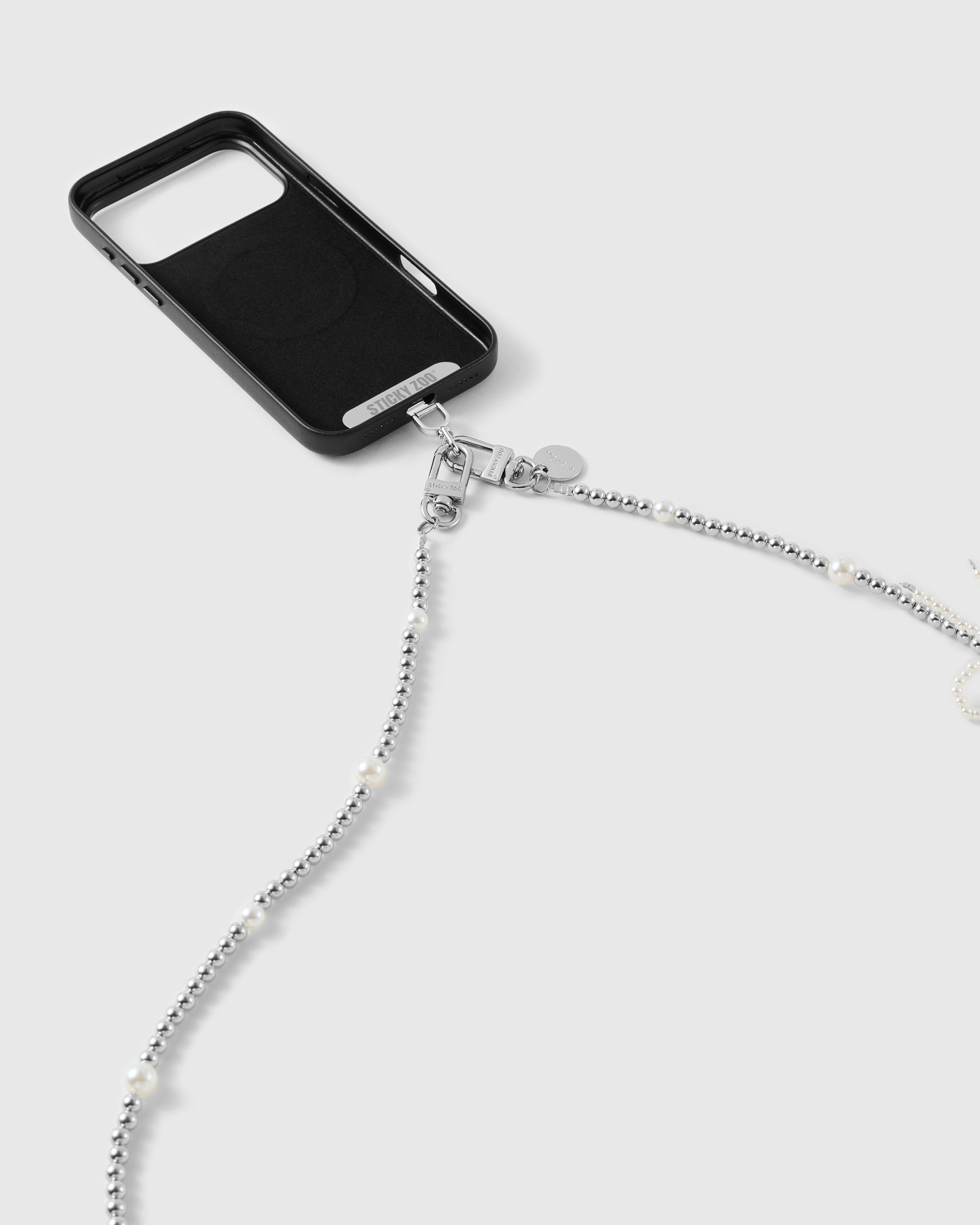 Dual silver-tone clasps and engraved disc connecting the faux-pearl beaded strap to a black phone case.